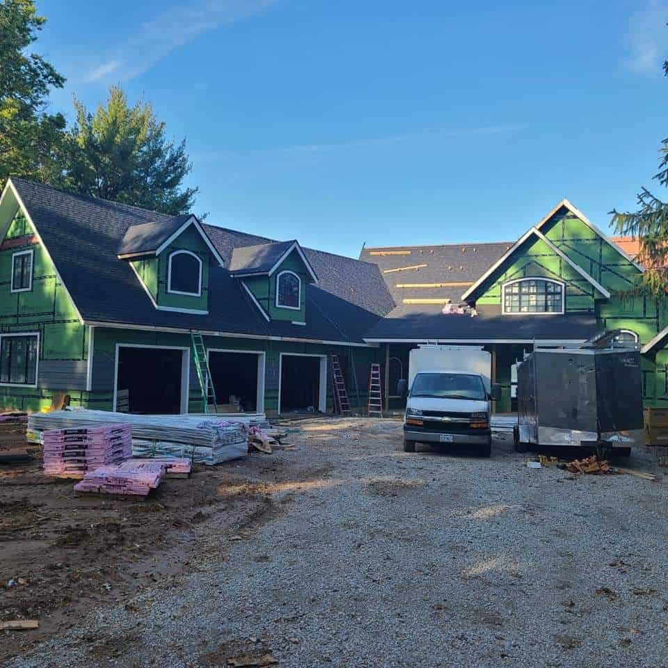 Residential construction site with a partially completed house, storm damage roofing materials, and building materials on the ground.
